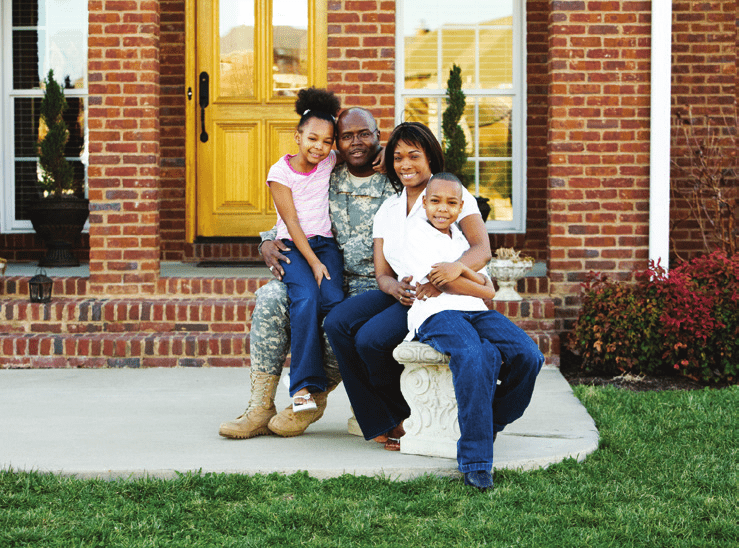Man in military uniform sitting with his family in front of home